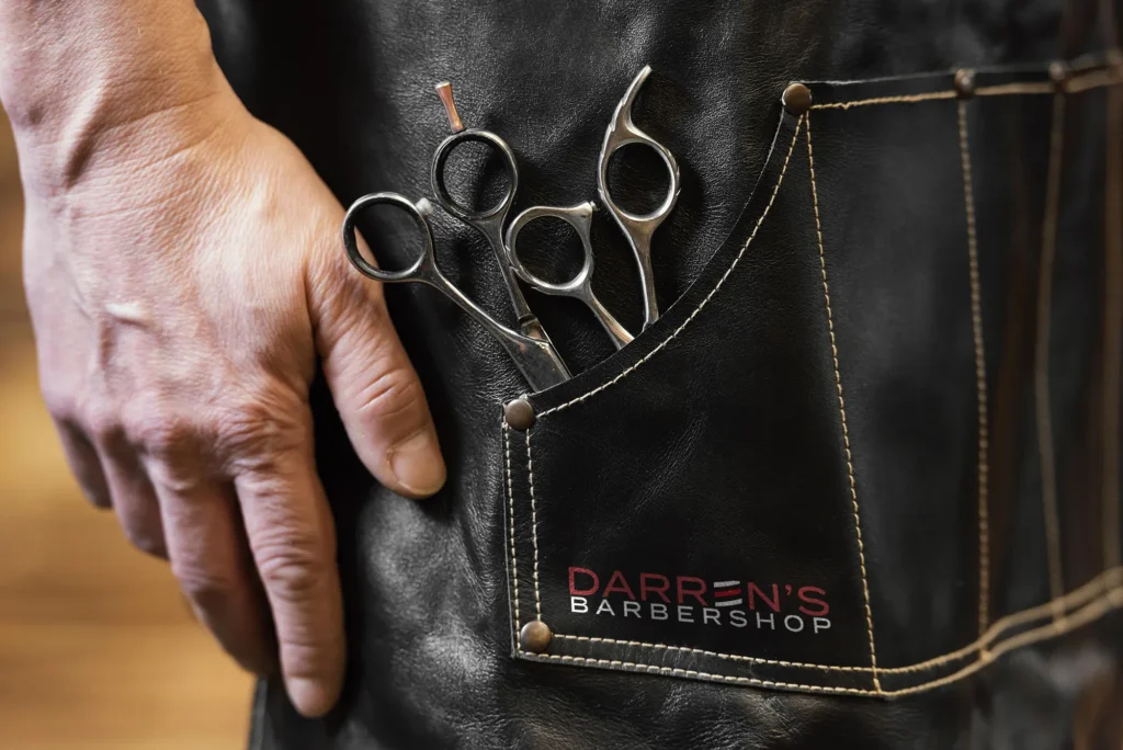 Barbershop logo design on branded apron pocket with scissors at Darren’s Barbershop