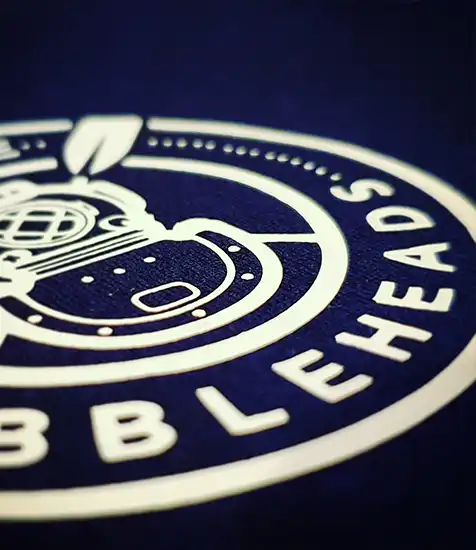 Close-up of custom printed Bubbleheads logo featuring a vintage diving helmet on navy fabric. Clothing printing supplier coventry