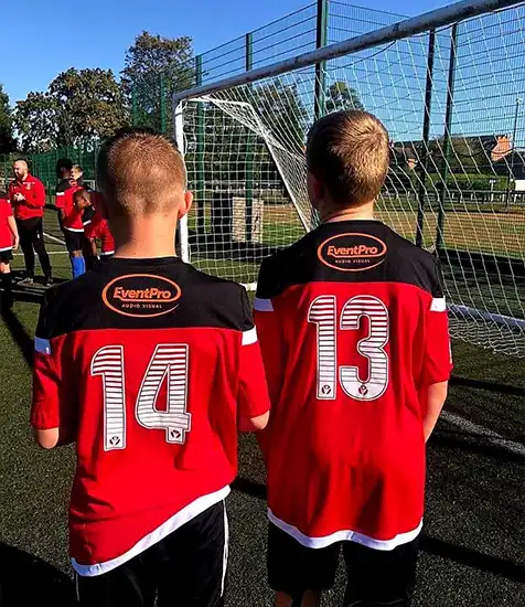 Custom clothing printing football shirts with player numbers and sponsor logo for a youth team on a sunny outdoor pitch.