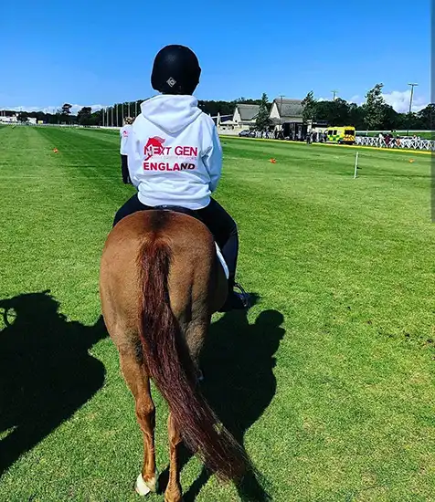 Rider wearing a custom clothing printed "Next Gen England" hoodie on horseback at a sporting event in the UK.