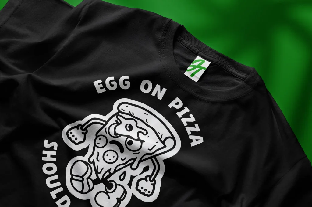 Black t-shirt mockup featuring a bold white cartoon-style pizza slice illustration with expressive character design and curved typography in a playful, streetwear-inspired layout